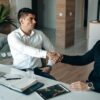 Two men shaking hands in an office, symbolizing successful agreement or partnership.